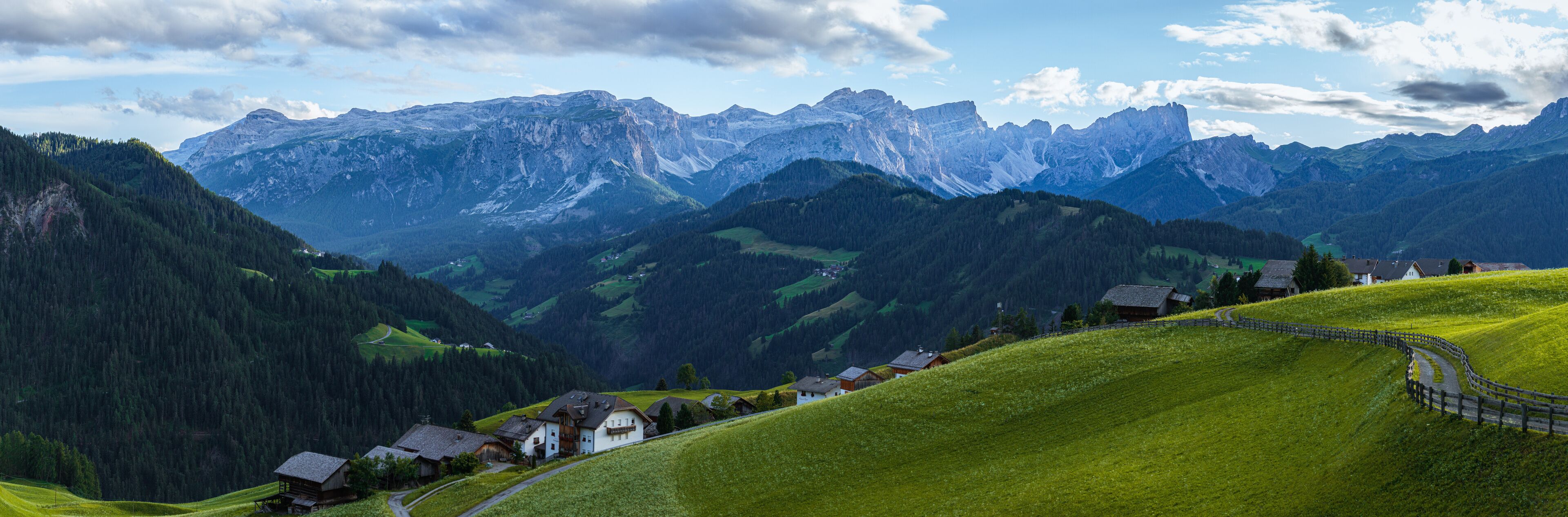 A mountainous landscape with a winding road, green fields, and traditional houses.