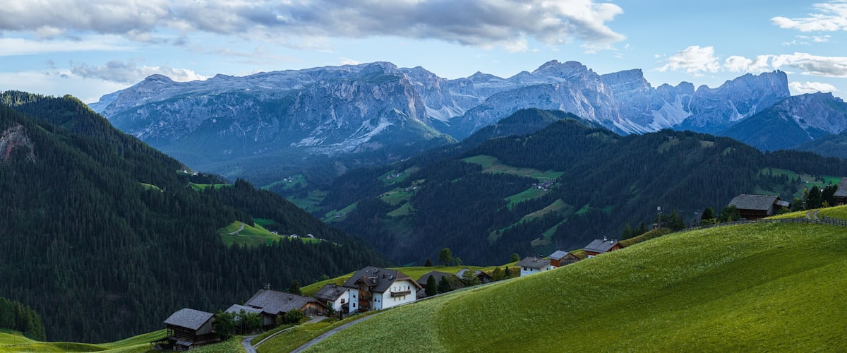 A mountainous landscape with a winding road, green fields, and traditional houses.