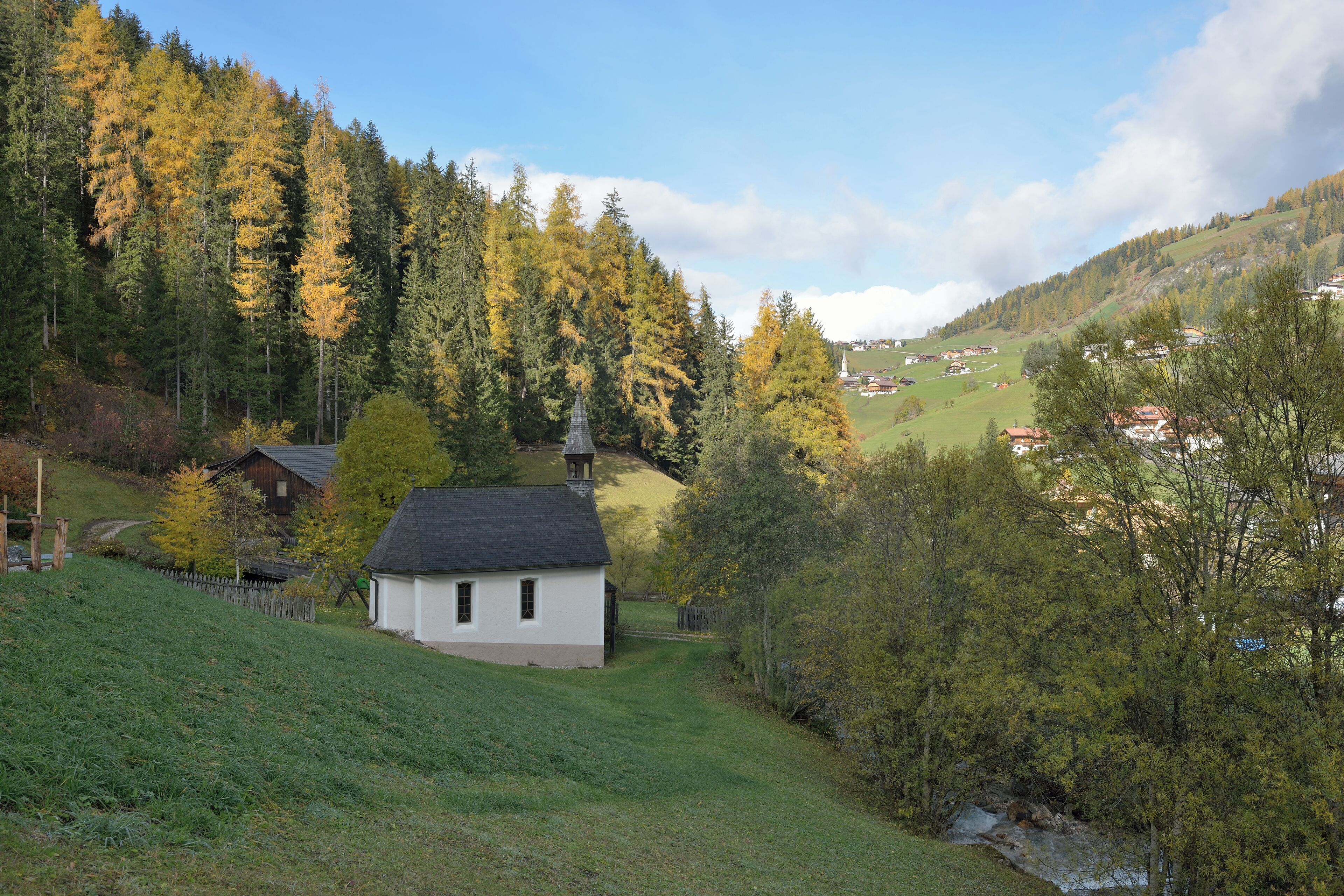 A small white house with a black roof surrounded by a forested hillside.