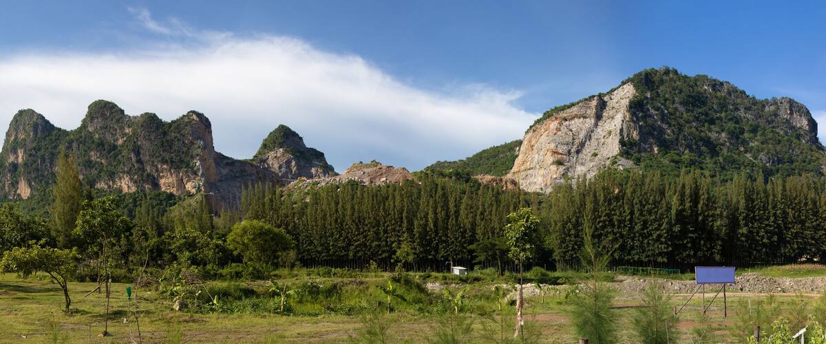 A mountainous landscape with a prominent rocky peak and a forested area in the foreground.