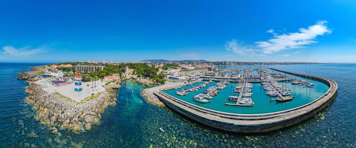 A coastal town with a marina, clear blue waters, rocky shoreline, and a lighthouse.