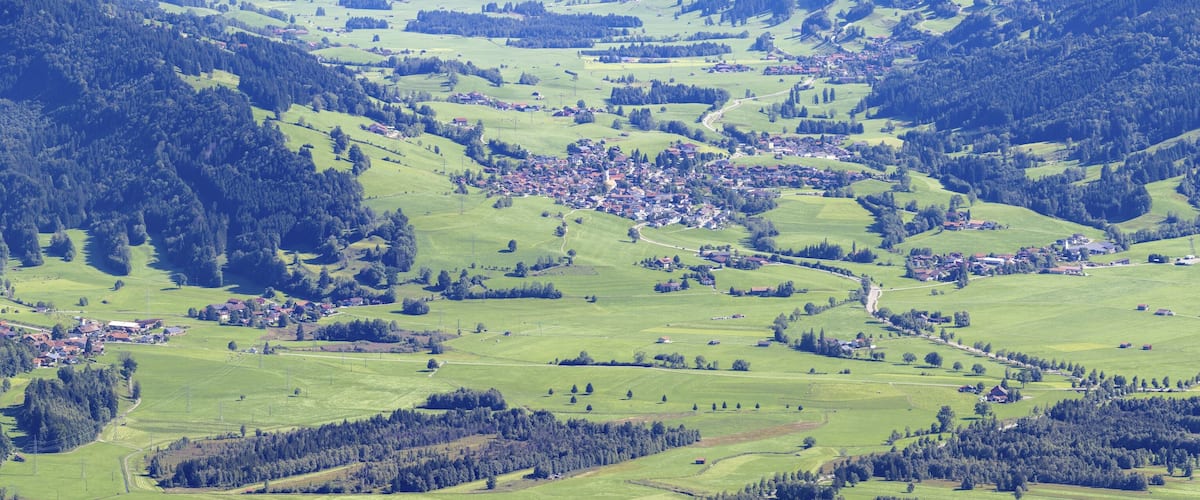 A valley with a small town surrounded by green fields and forested hills.