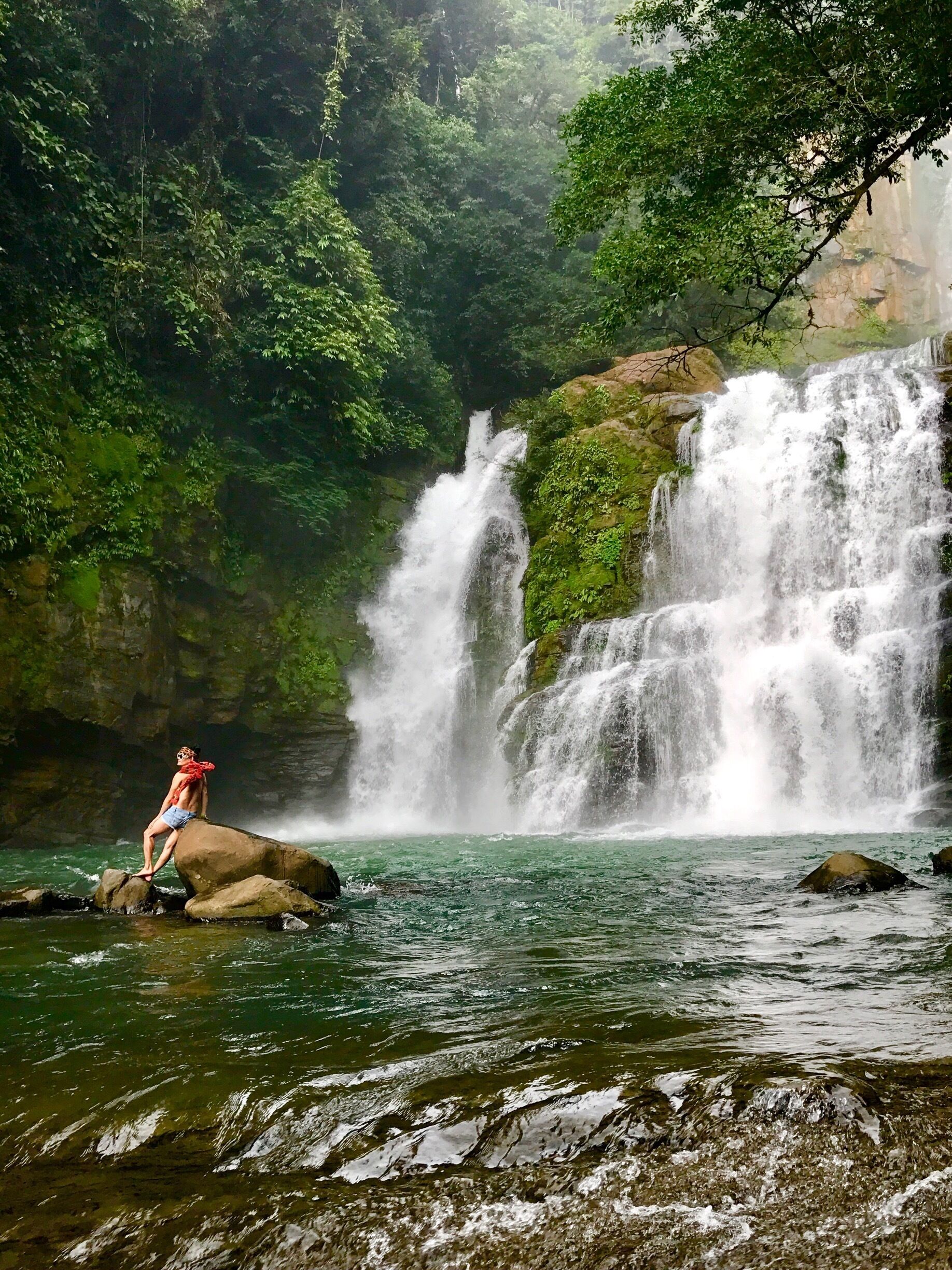 A waterfall cascading over rocks into a river surrounded by dense forest.