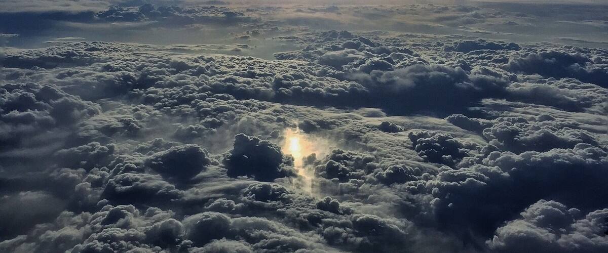 A view of clouds from above with a bright light source in the distance.