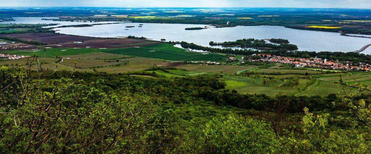 A panoramic view of a river valley with fields, a small town, and a cloudy sky.