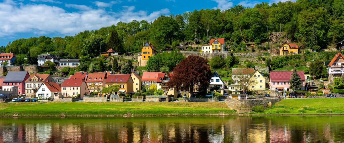 A lakeside village with colorful houses, a bridge, and a forested hillside.