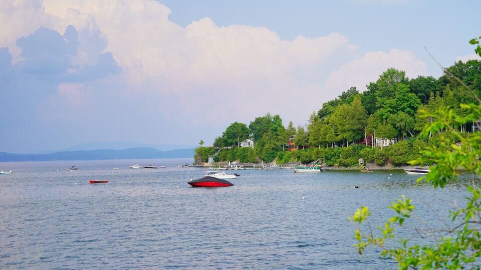 A calm lake with several boats, surrounded by lush greenery and trees.