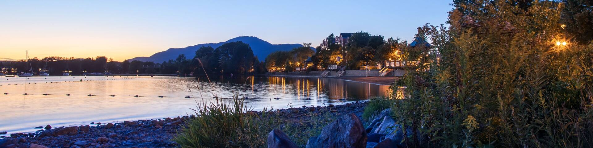 Beautiful Magog town at night in reflections of Memphremagog lake. Canadian romantic landscape with mountains, lake, night sky and awesome water background.