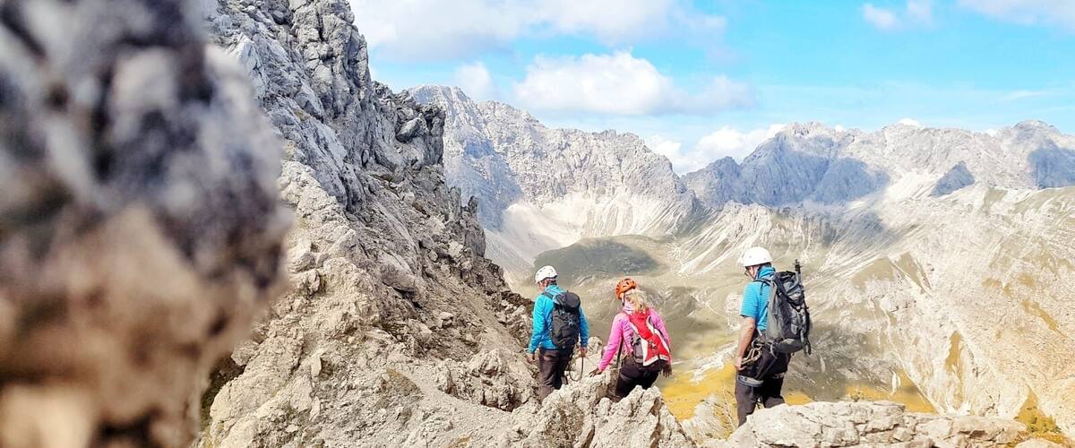 A group of hikers on a rocky mountain trail with a valley in the background.