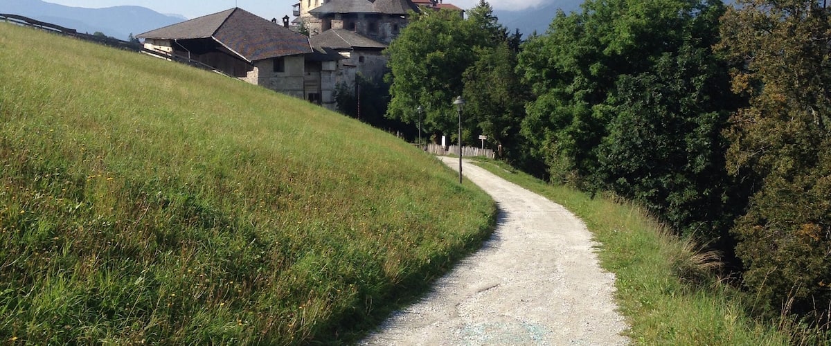 A gravel path leading to a building with a red roof, surrounded by greenery and mountains in the background.