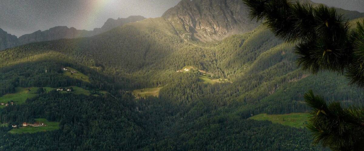 A mountain range with a rainbow and a forested valley.