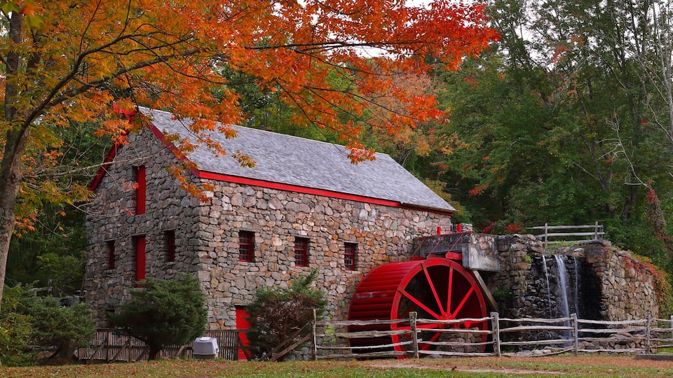 A stone building with a red roof and a large red water wheel.