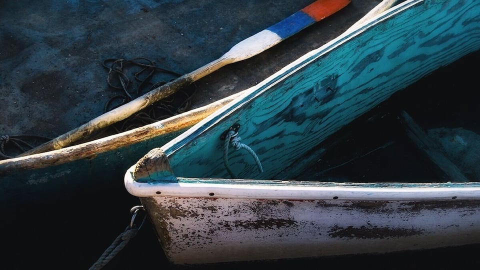 A weathered boat with a rope and a wooden oar.