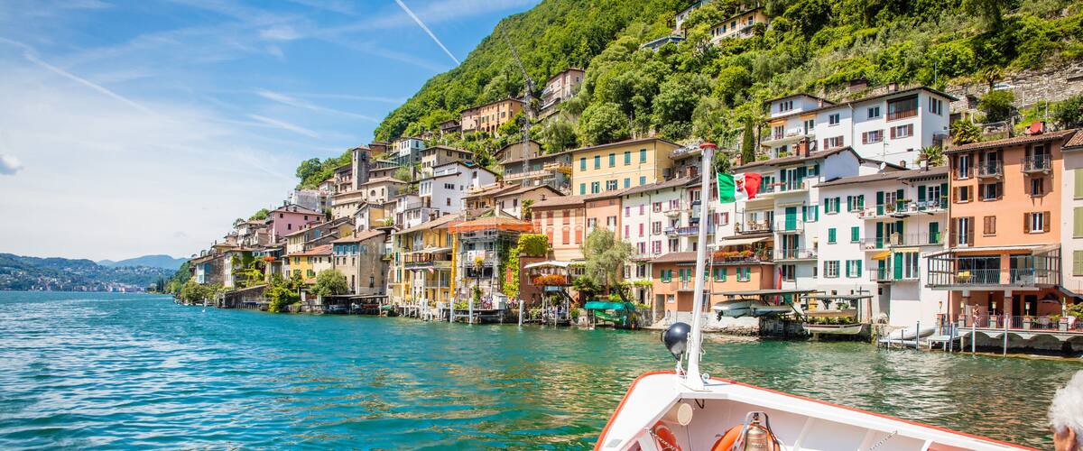 A boat on a calm lake with colorful buildings on the shore.