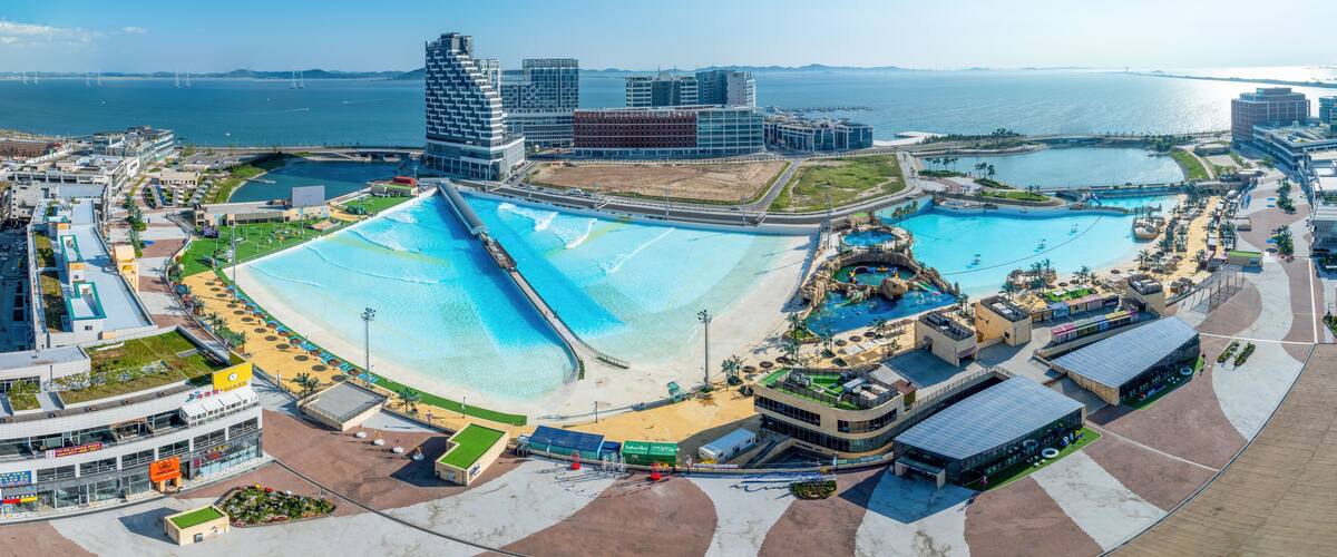 A coastal cityscape with a large artificial beach, modern buildings, and a marina.