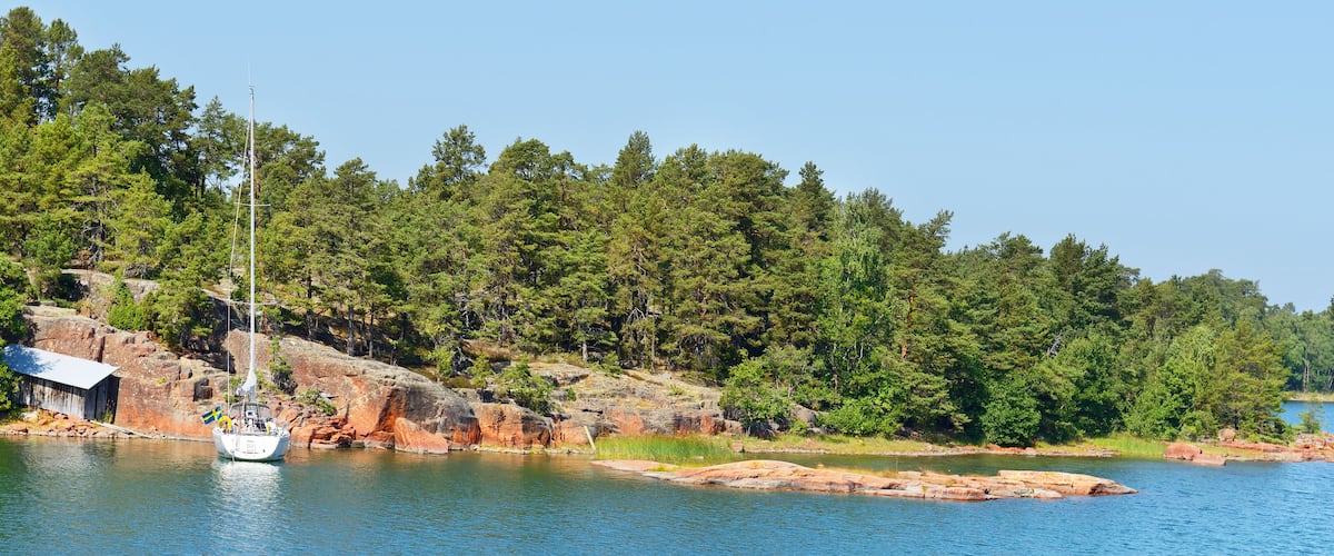 A sailboat on a calm lake with a forested shoreline and a small building.