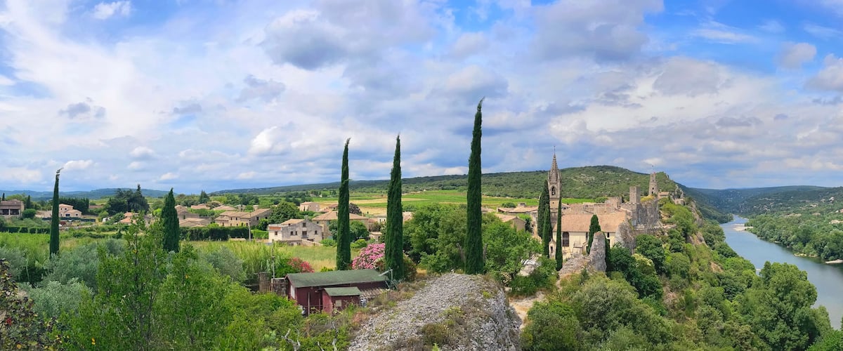 A village with a river, tall cypress trees, and a castle-like structure.