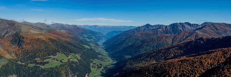 Une vallée où les arbres arborent les couleurs de l’automne, une rivière et des chaînes de montagnes.