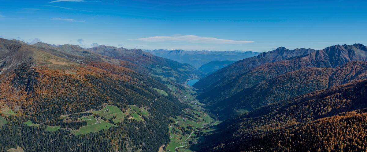 A valley with autumn-colored trees, a river, and mountain ranges.