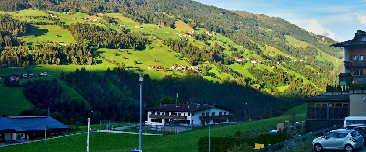 A mountainous landscape with green fields, scattered houses, and a building with a sloped roof.