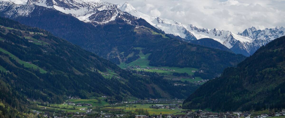 A valley with a small town surrounded by mountains and snow-capped peaks.