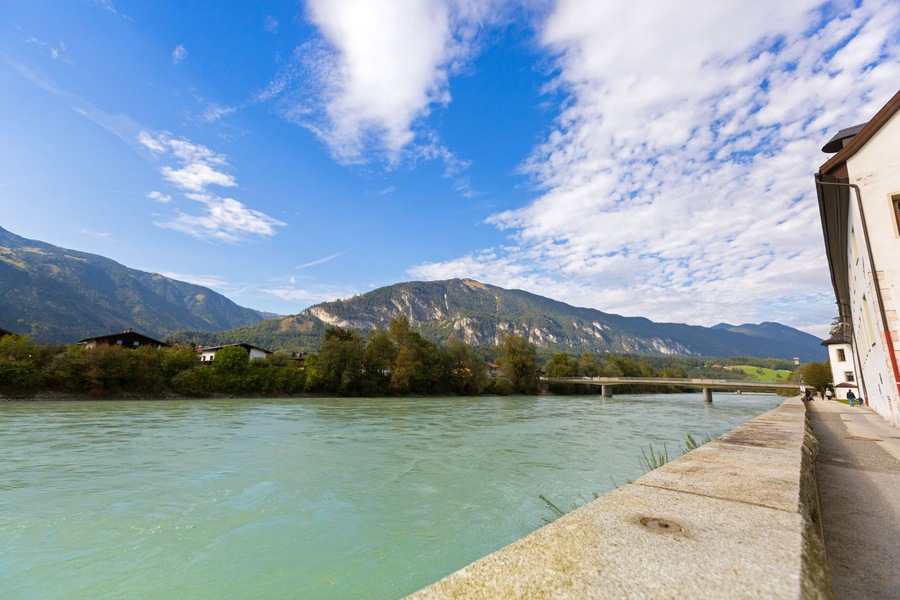 Waterfront view of Inn river along Inn promenade with mountain, blue sky in Rattenberg, Austria, Europe.