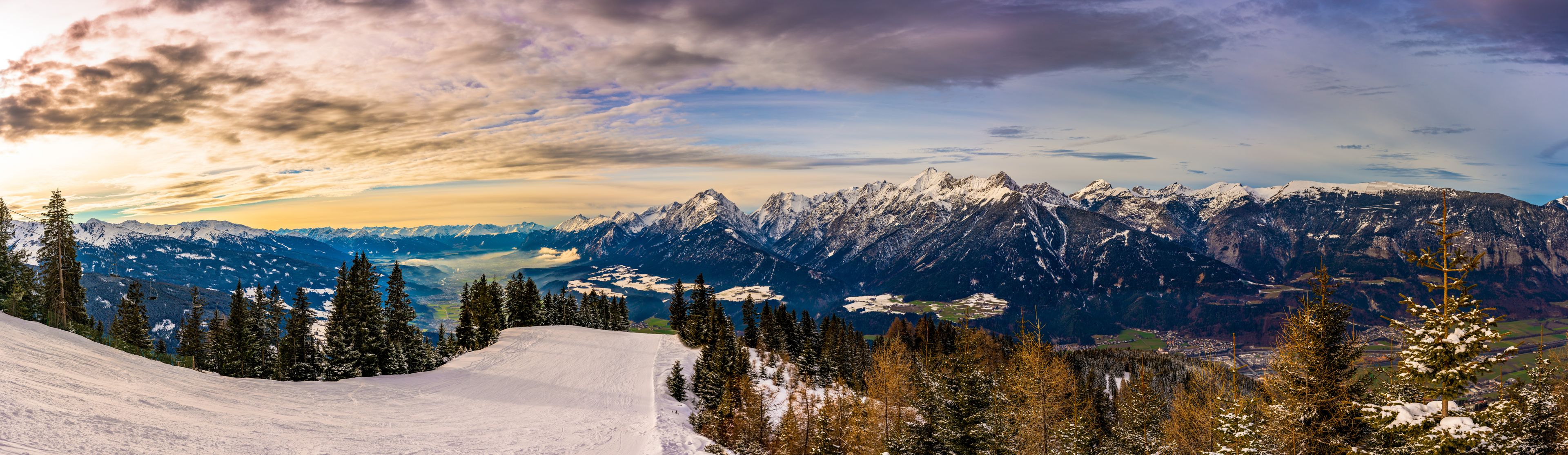A snow-covered mountain range with a ski slope and trees.