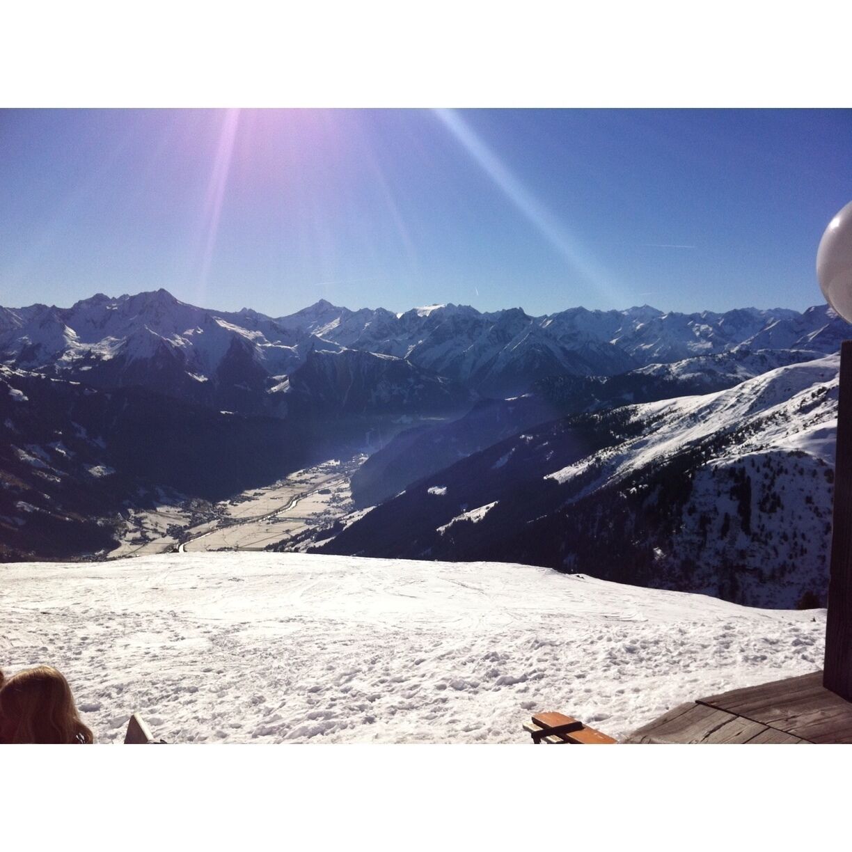 A snowy mountain landscape with a clear sky and a sun shining from the left.