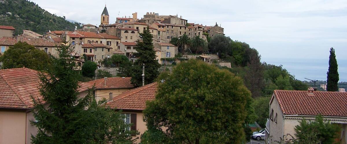 A hillside town with terracotta-roofed buildings, a church steeple, and lush greenery.