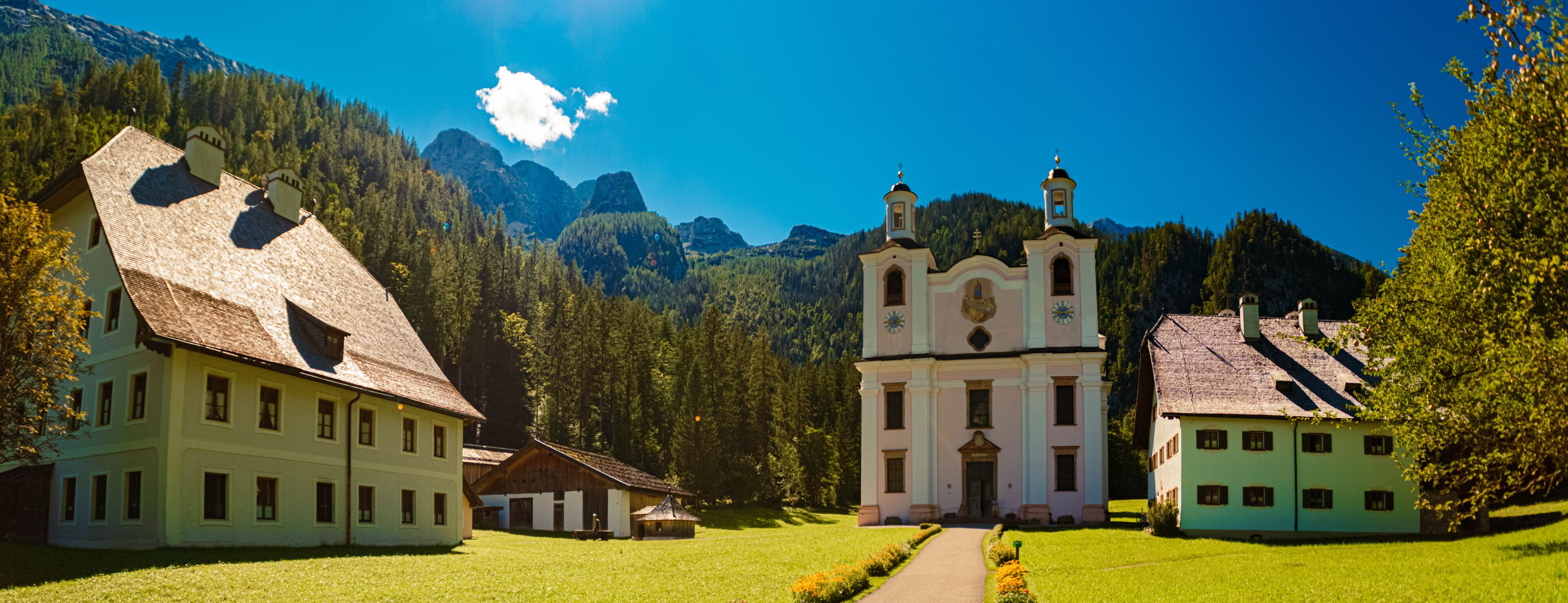 A church with a bell tower, surrounded by lush greenery and mountains in the background.