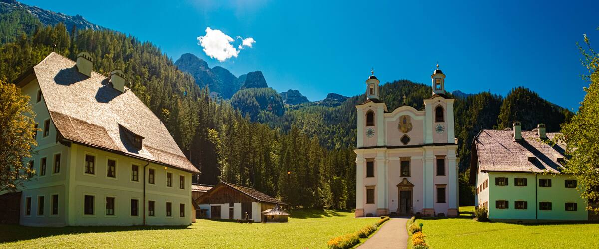 A church with a bell tower, surrounded by lush greenery and mountains in the background.