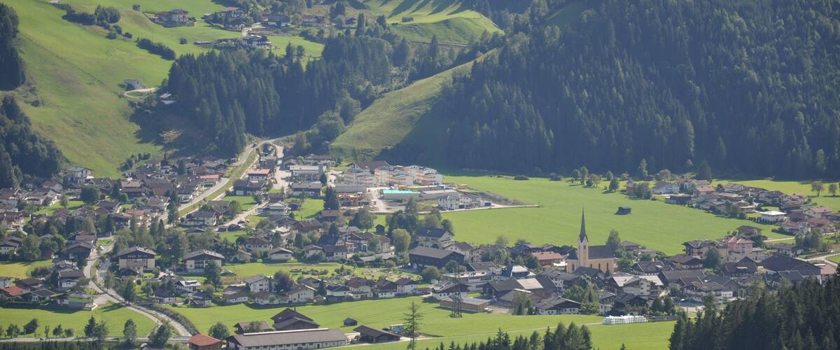 A rural village nestled in a valley with a church, surrounded by green fields and forested hills.