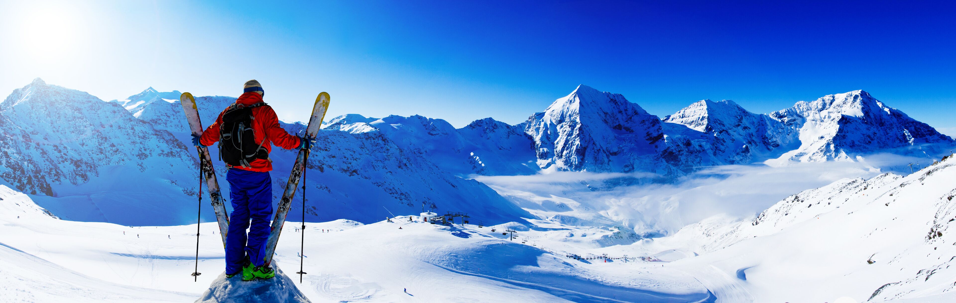 Mountaineer backcountry ski resting along a snowy ridge with skis in the backpack. In background blue sky and shiny sun and Ortler in South Tirol, Italy.  Adventure winter extreme sport.
