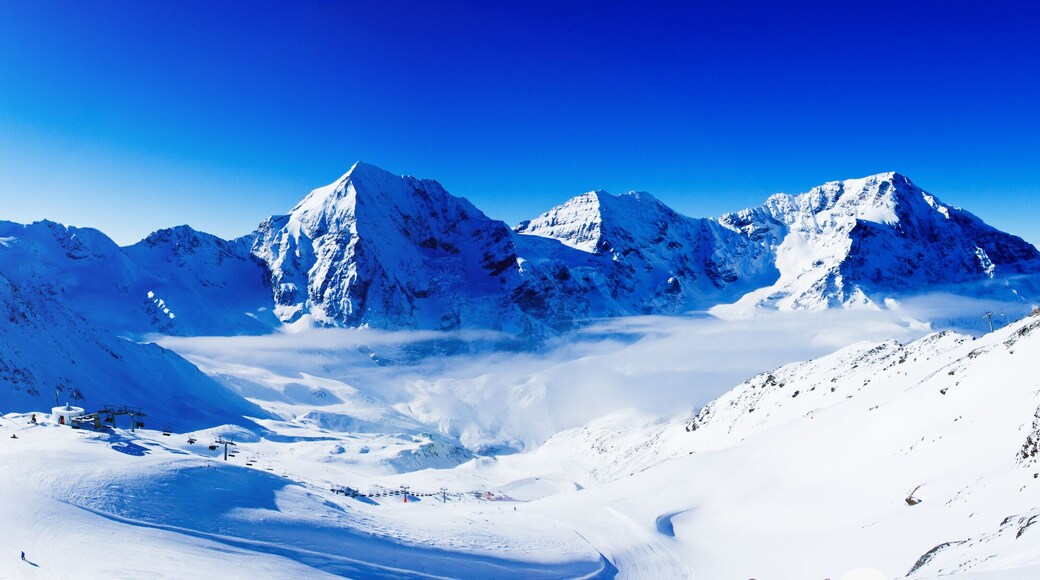 Mountaineer backcountry ski resting along a snowy ridge with skis in the backpack. In background blue sky and shiny sun and Ortler in South Tirol, Italy. Adventure winter extreme sport.