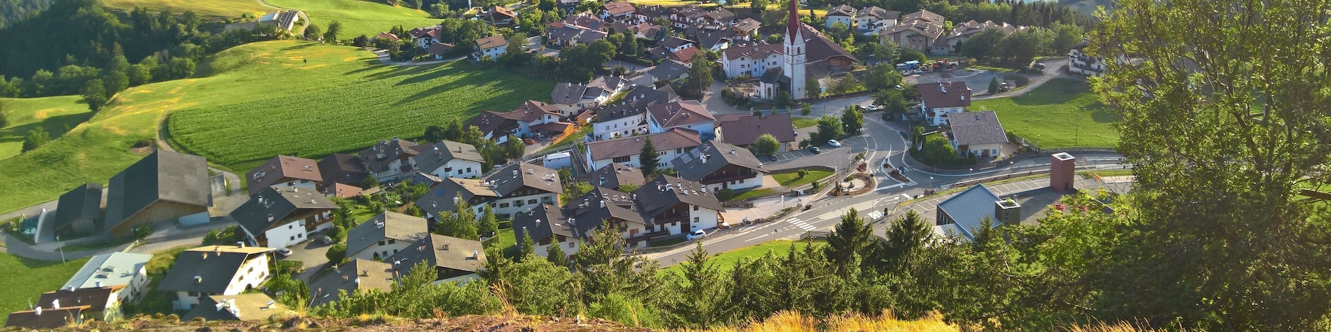 A mountainous town with a prominent church, surrounded by lush green fields and a river.