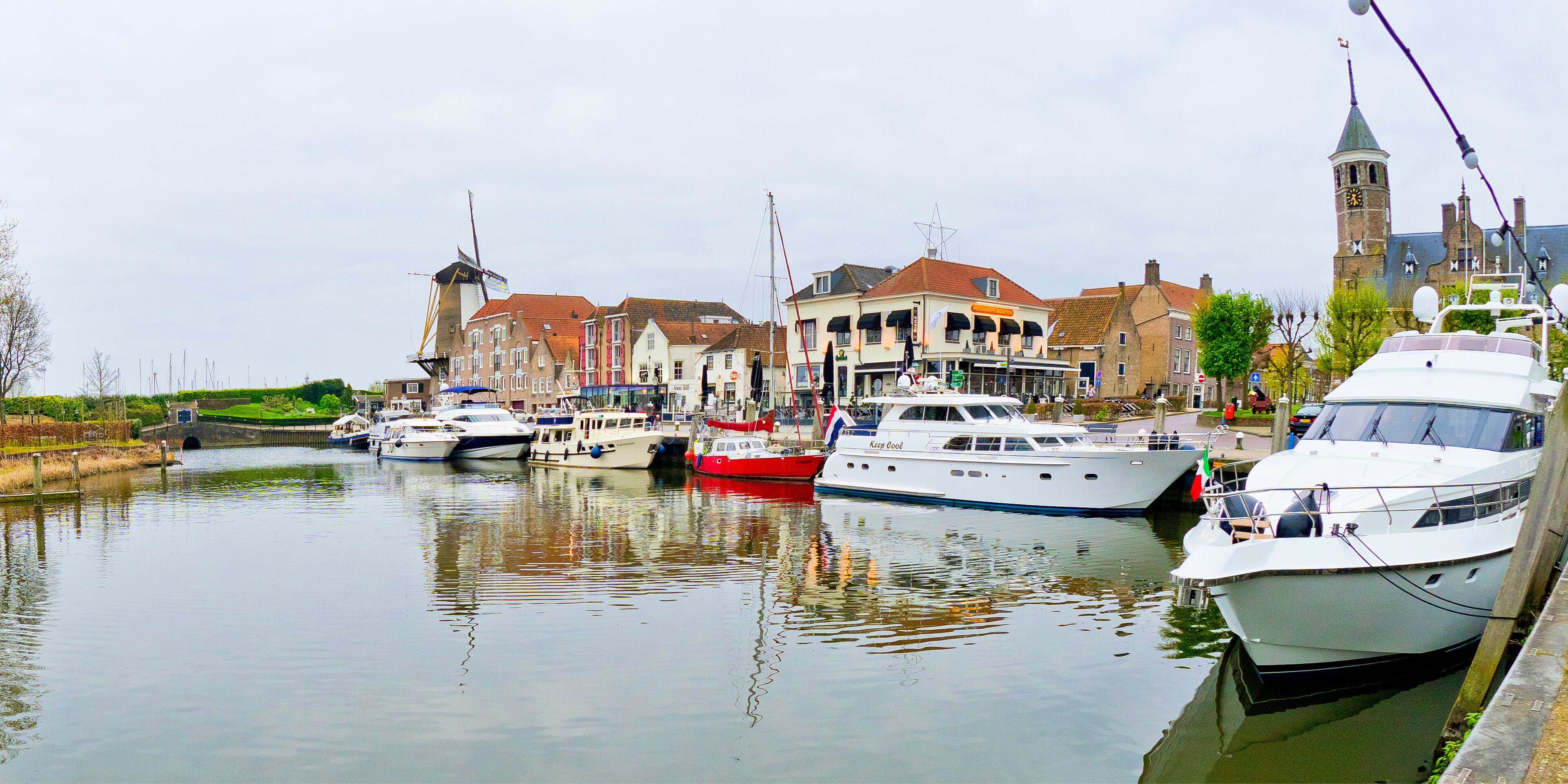A canal with boats docked, a windmill, and historic buildings.