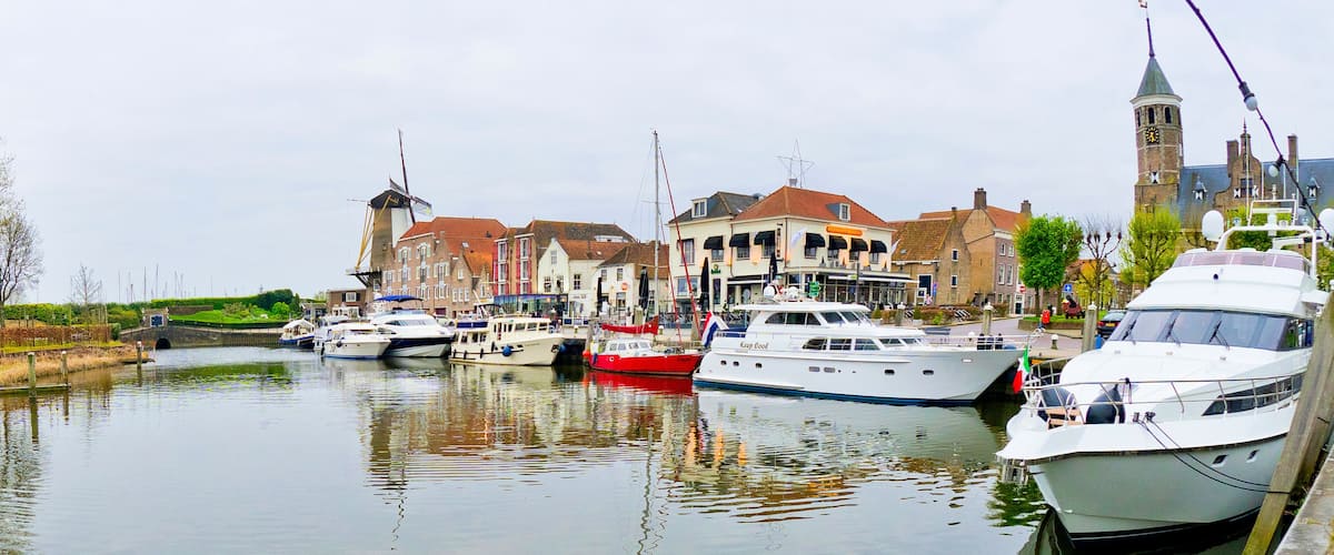 A canal with boats docked, a windmill, and historic buildings.