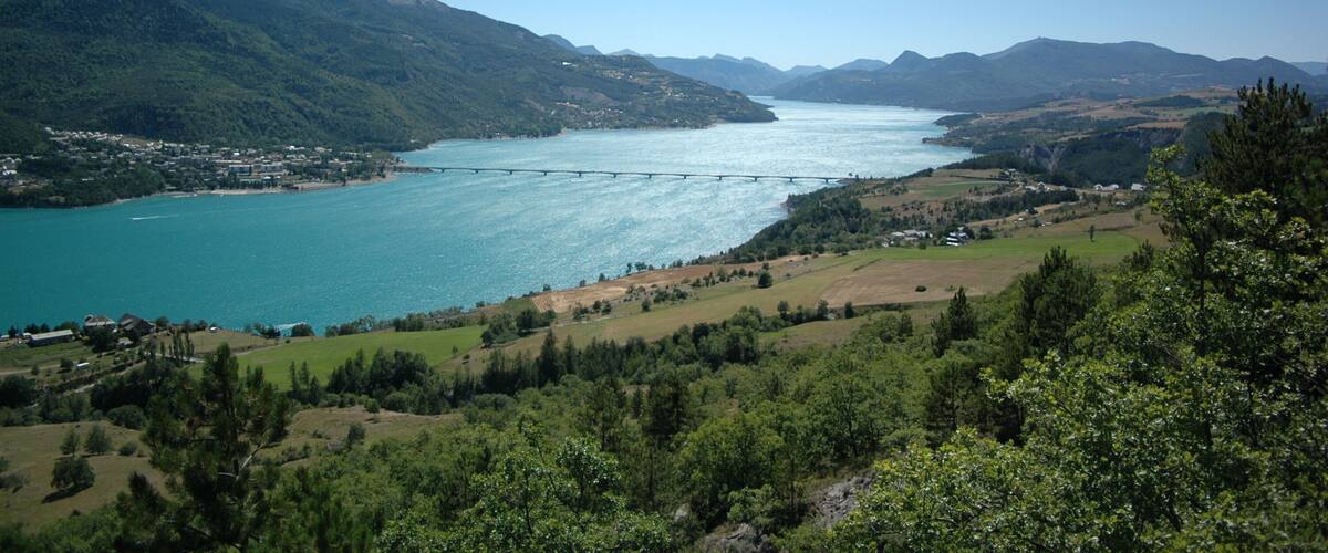 A mountainous landscape with a lake, a bridge, and scattered buildings.