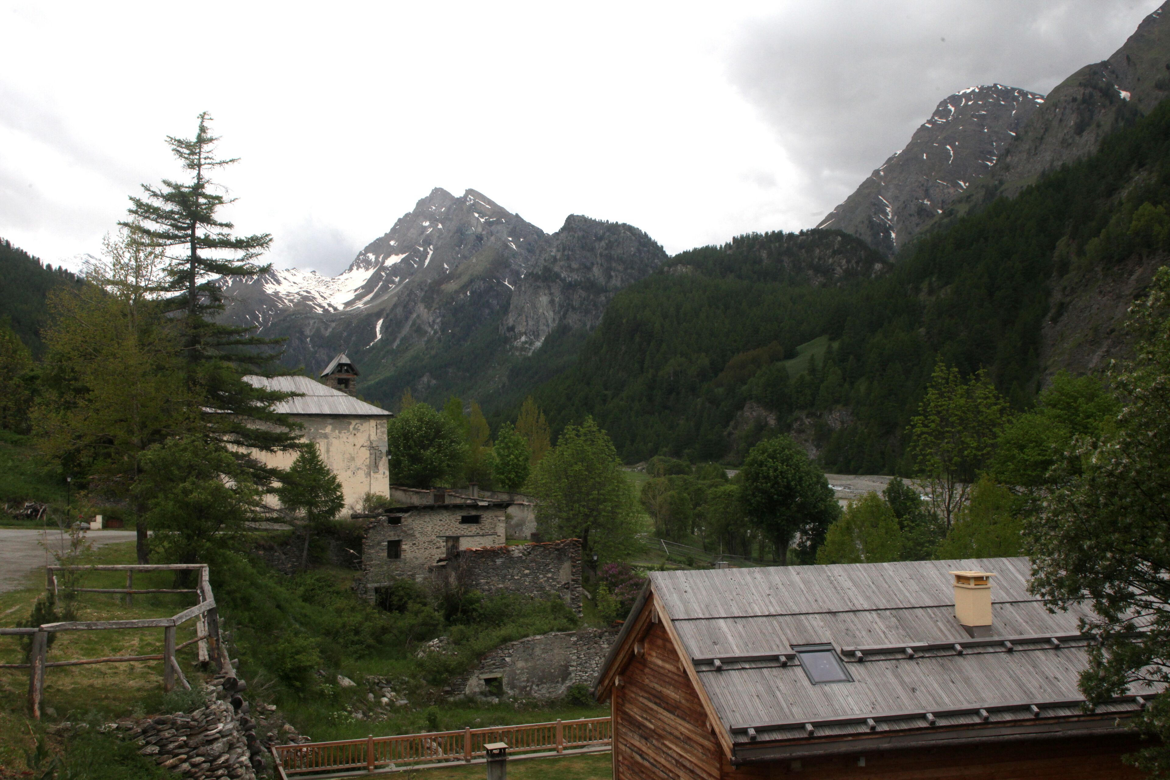 A mountainous landscape with a wooden cabin, a stone building, and a forested area.