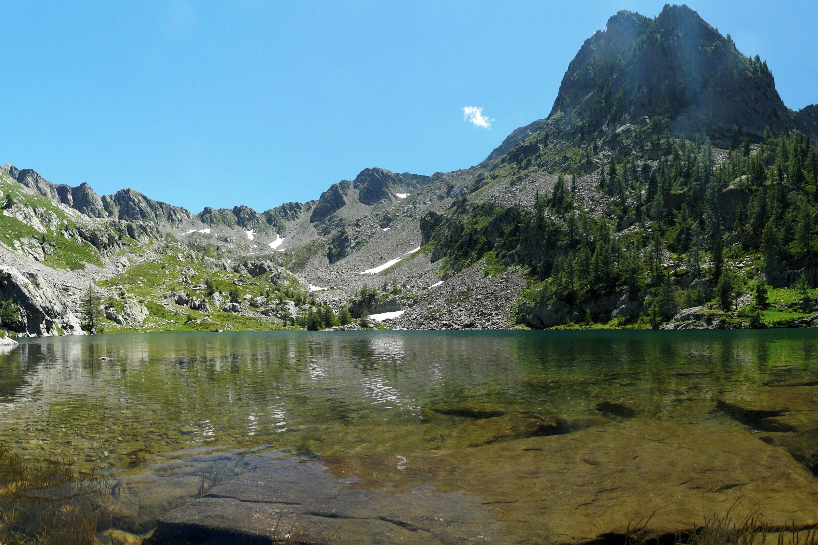 A clear mountain lake surrounded by rugged peaks and dense forest.