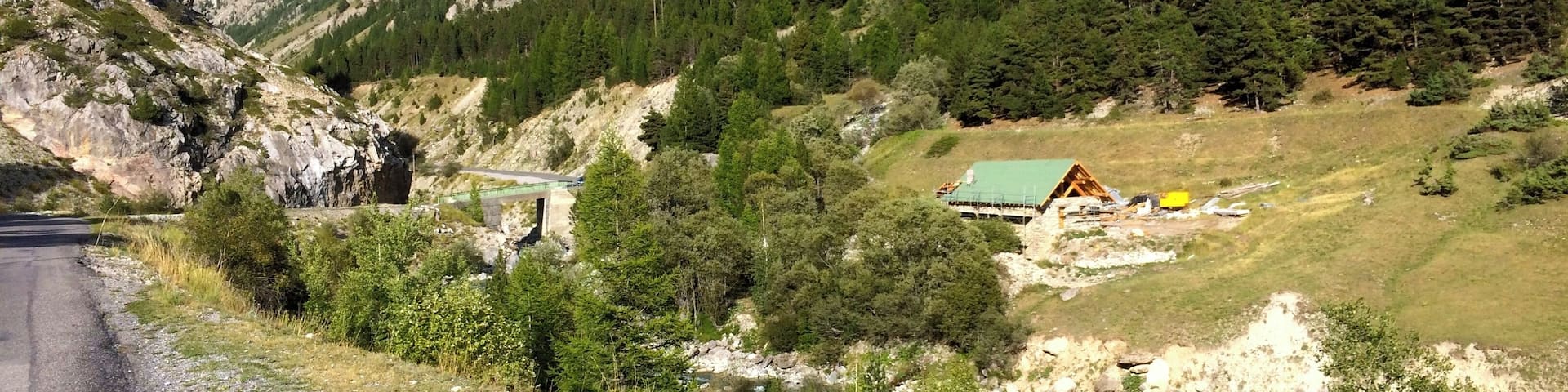 A mountain road with a small house and a bridge in the valley.