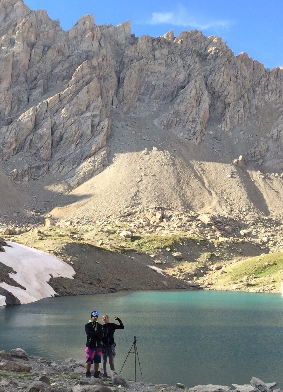 A mountainous landscape with a clear lake, rocky terrain, and a tripod.