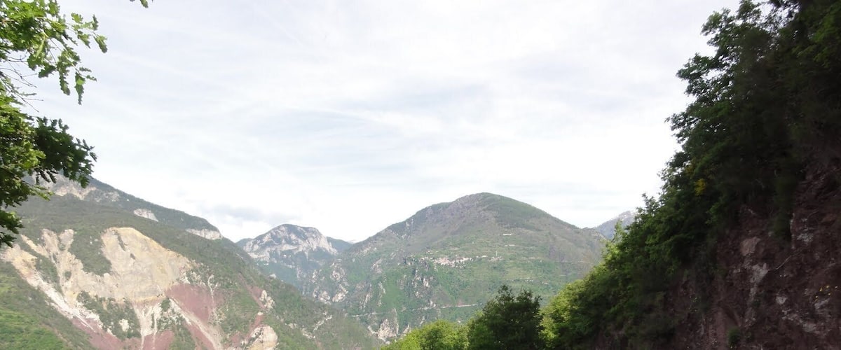 A mountainous landscape with a dirt path, green vegetation, and rocky cliffs.