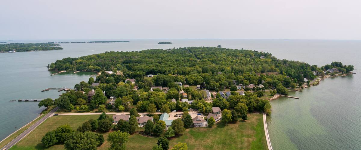 An aerial view of a densely wooded island with residential houses, surrounded by calm water.