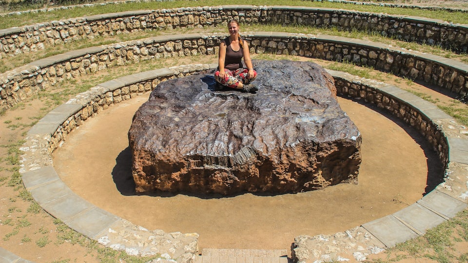 The largest meteorite in the world at Grootfontein, Namibia. A huge piece of iron from space. White girl tourist sitting on a meteorite