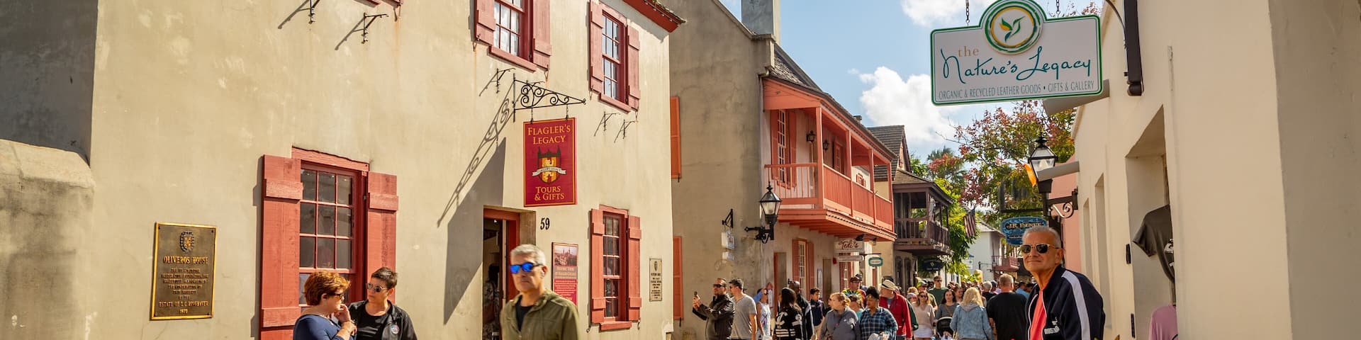 A bustling street with historic buildings, a sign for 'The Nature's Legacy' shop, and a plaque for 'Oliver's House'.