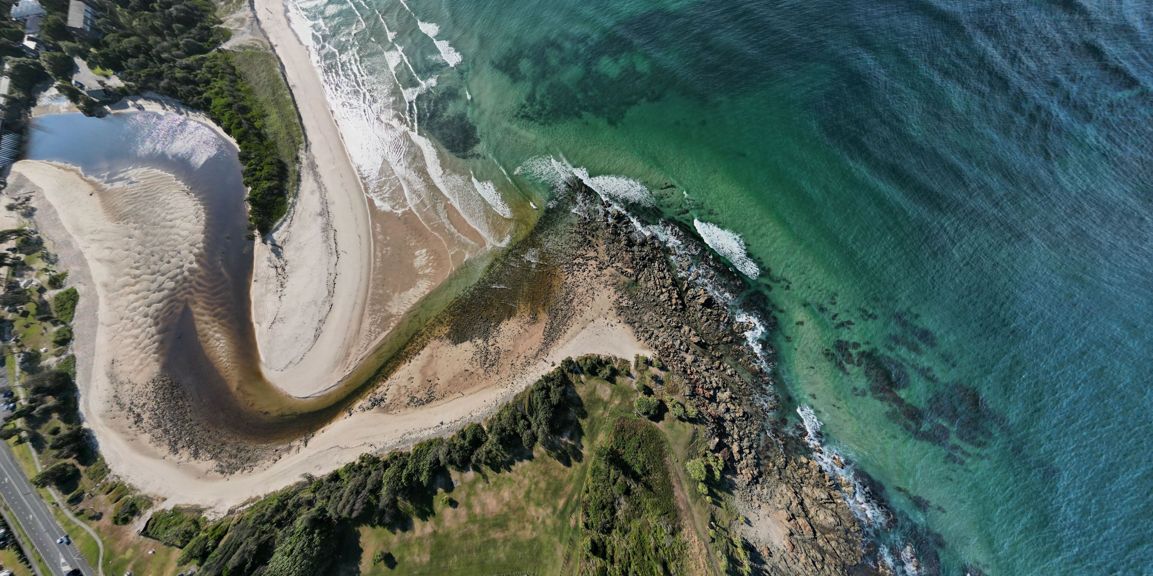 An aerial view of a coastal area with a sandy beach, rocky shoreline, and clear turquoise waters.