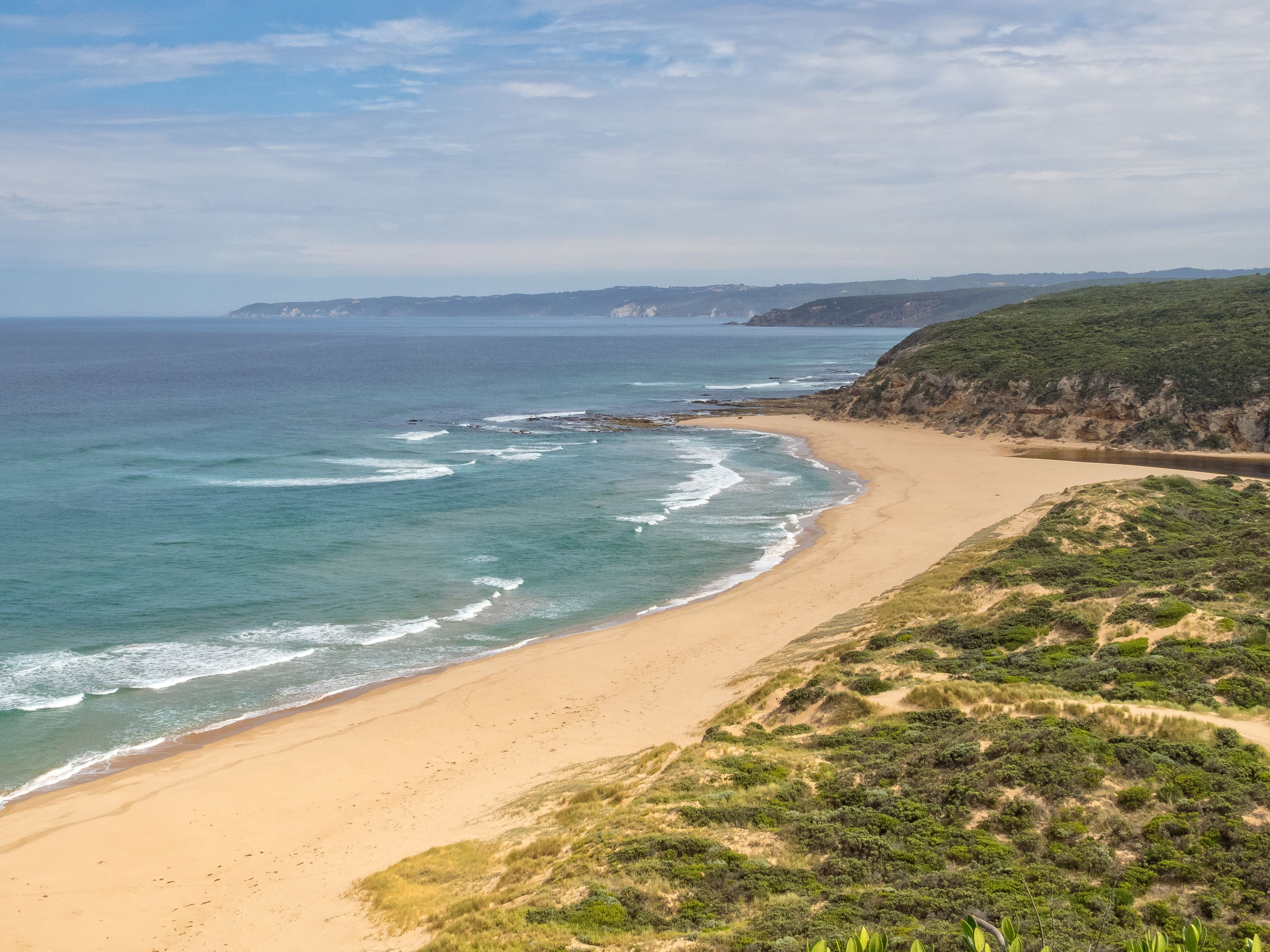 A coastal landscape with a sandy beach, ocean waves, and a green hillside.