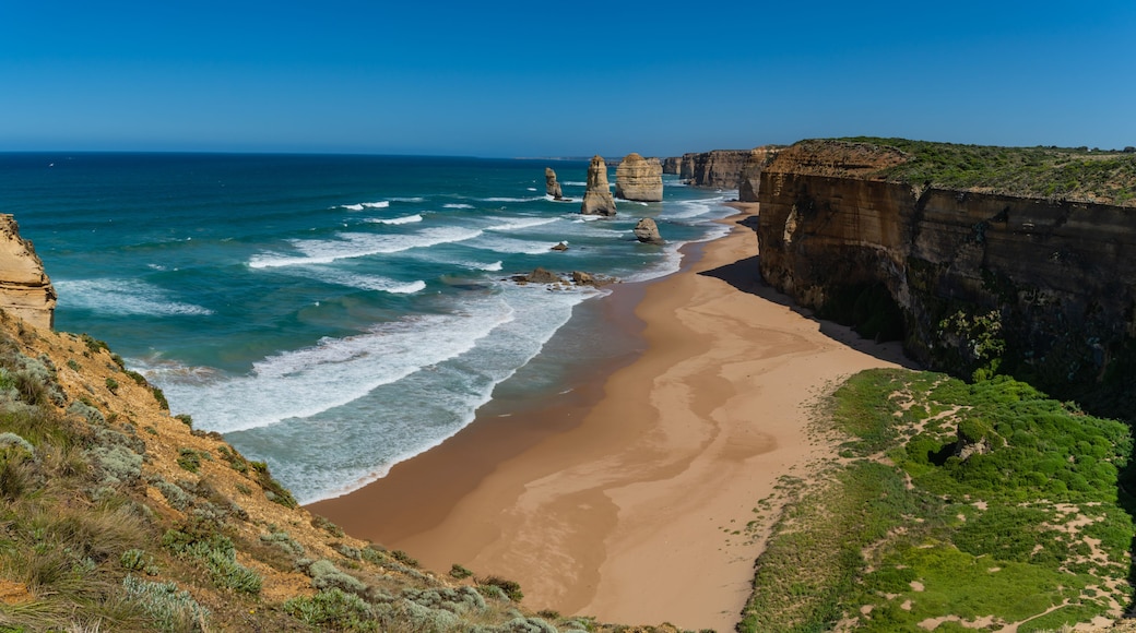 A coastal landscape with a sandy beach, towering rock formations, and a clear blue sky.