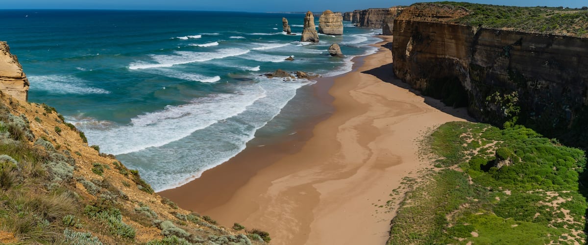 A coastal landscape with a sandy beach, towering rock formations, and a clear blue sky.